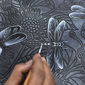 Hand etching a floral pattern onto an Anuschka Round Coin Purse - 1175 with a white pencil.