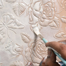 Load image into Gallery viewer, Hand applying paint on a raised floral relief pattern on an Anuschka Large Zip Top Tote - 698.
