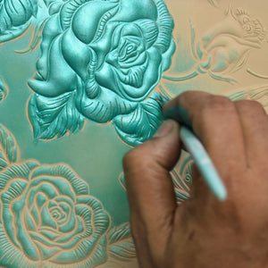 Hand etching intricate floral patterns on a teal-colored Anuschka Large Zip Top Tote - 698.