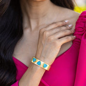 A woman showcasing a Triangle Druzy Bracelet - VBR0002 by Vanya Lara, with blue Druzy gemstone inlays, against a pink garment.