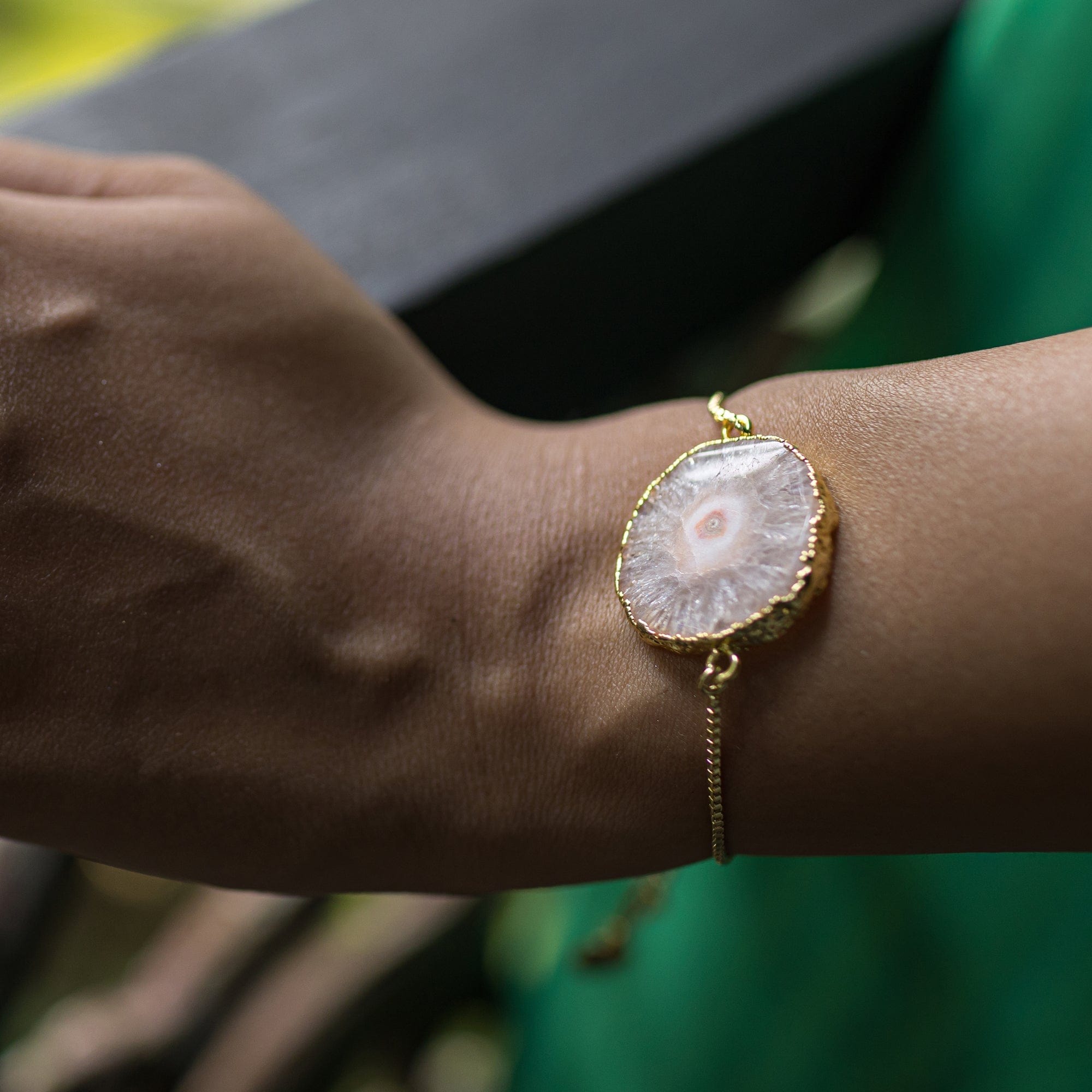 A woman's wrist adorned with a unique, Sliced Quartz Bracelet by Vanya Lara against a green fabric background.