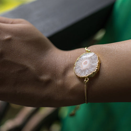A woman's wrist adorned with a unique, Sliced Quartz Bracelet by Vanya Lara against a green fabric background.