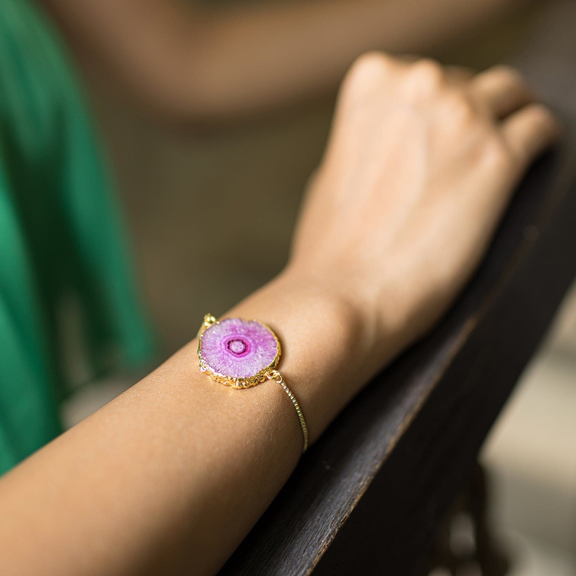 A woman's wrist adorned with a Vanya Lara gold-plated Sliced Quartz Bracelet featuring a large purple gemstone centerpiece.