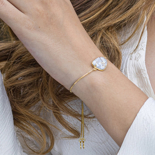 A woman wearing a Mojave Glory Bracelet (VBR0005) from her Vanya Lara jewelry collection with a white marbled charm and a dangling key pendant.