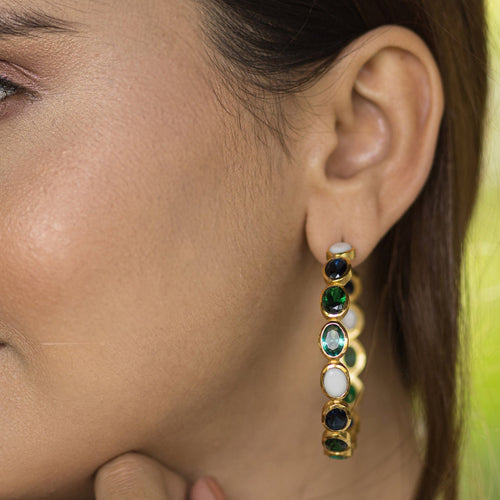 Close-up of a woman's ear wearing Vanya Lara Kaleidoscope Hoop Earrings - VER0002 with green, blue, and white stones.