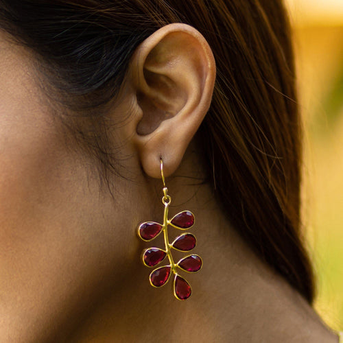 A close-up of a woman's ear wearing Vanya Lara's Foliage Earrings - VER0005 with red gemstones and an eye-catching, unique design.