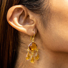 Load image into Gallery viewer, A close-up of a woman&#39;s ear wearing Vanya Lara&#39;s Triple Dew Drop Earrings with amber-colored hydro stone setting.
