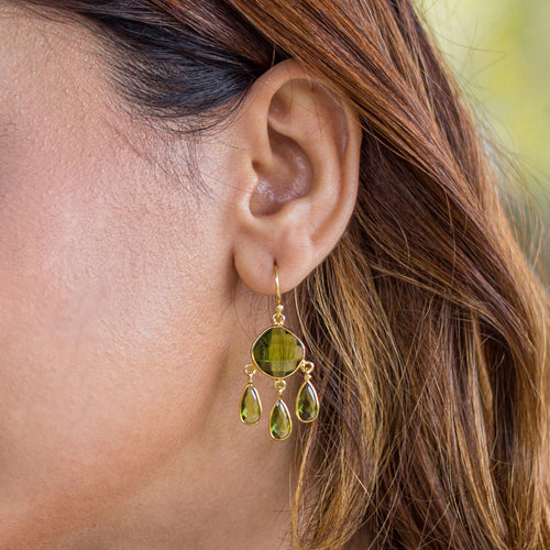 A close-up of a woman's ear wearing Vanya Lara's Triple Dew Drop Earrings - VER0006 with green gemstones.