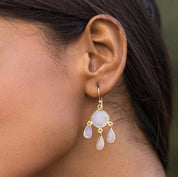 A close-up of a woman's ear wearing Vanya Lara's Triple Dew Drop Earrings with hydro stone settings and three teardrop gems.