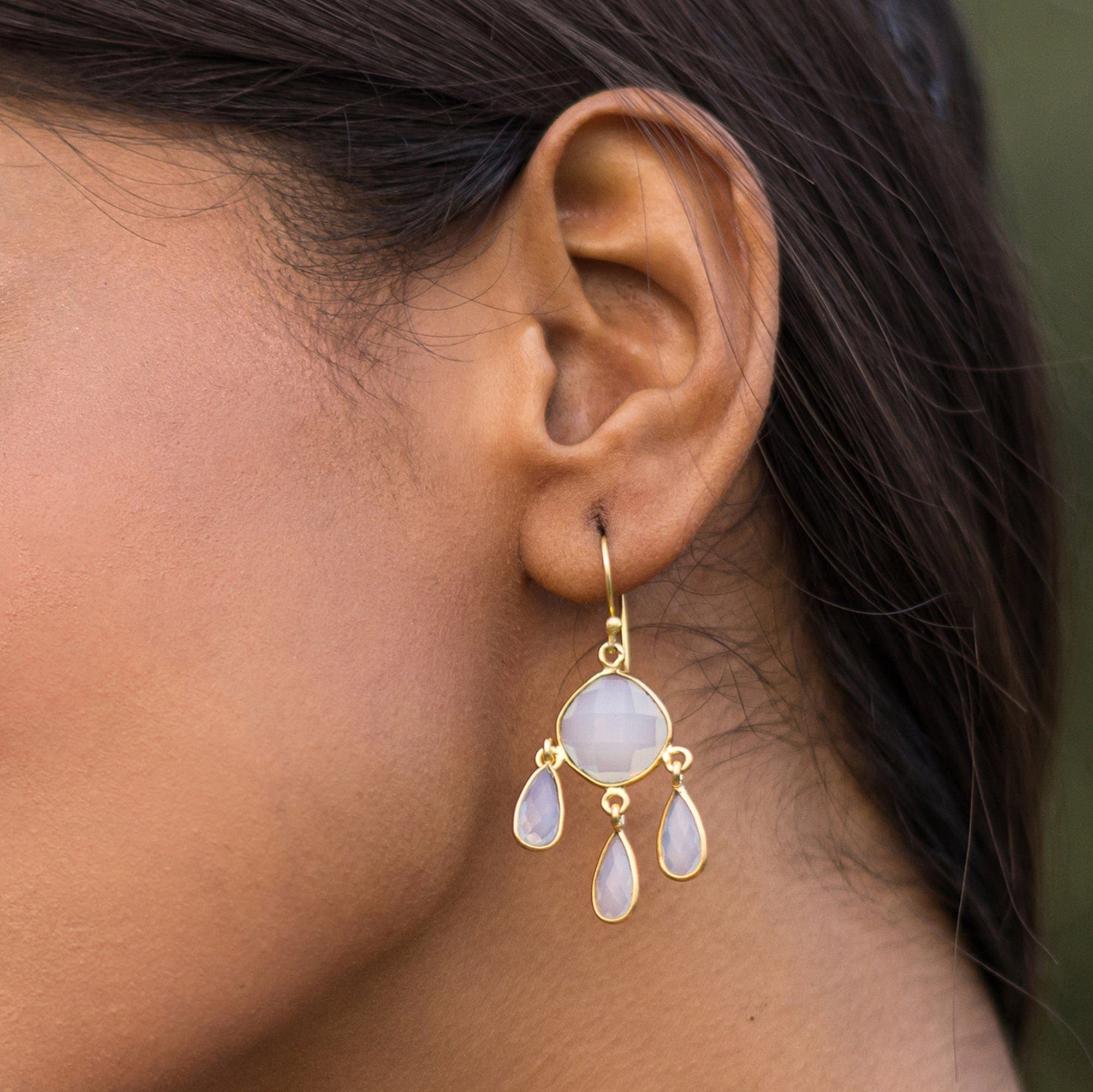 A close-up of a woman's ear wearing Vanya Lara's Triple Dew Drop Earrings with hydro stone settings and three teardrop gems.