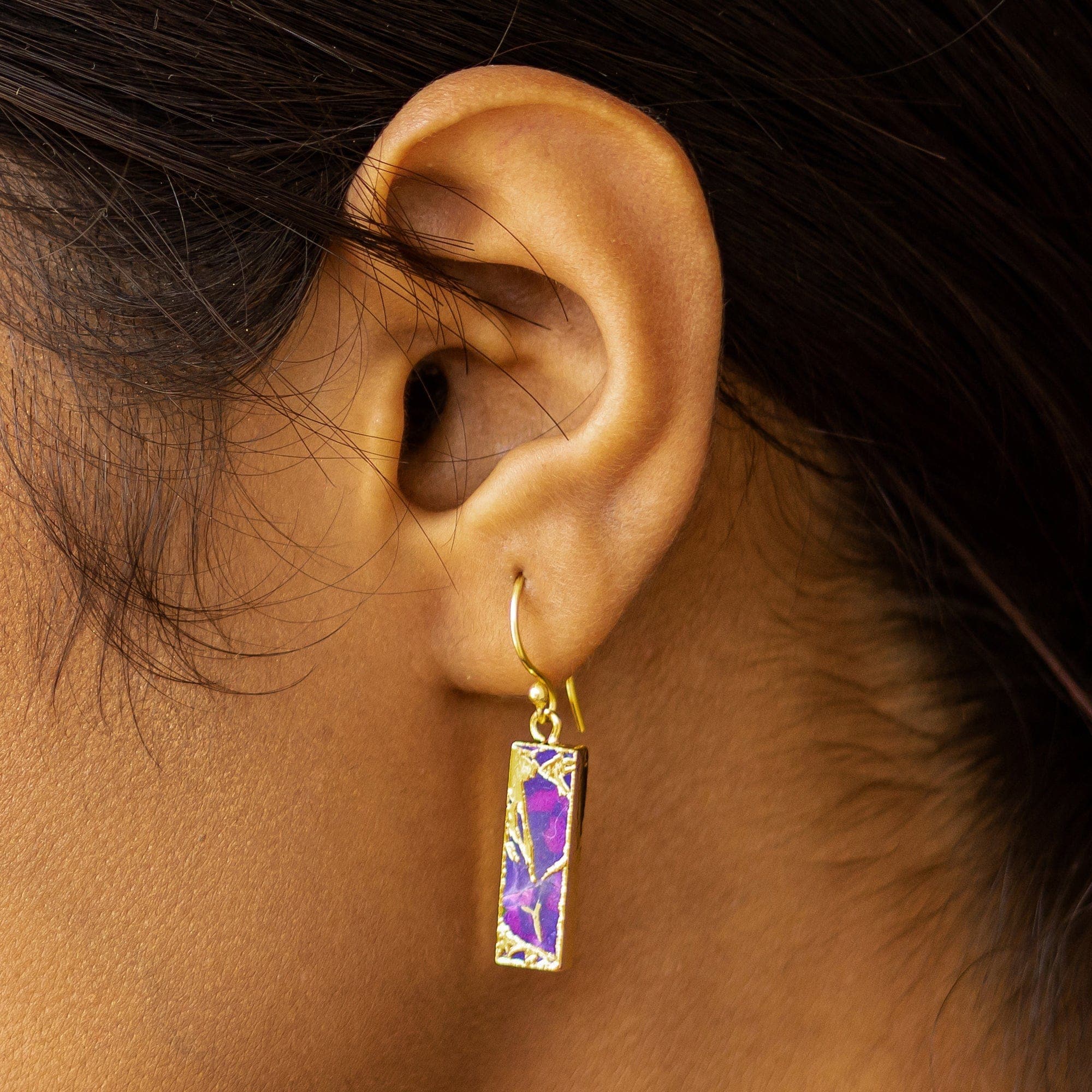 A close-up of a person's ear showcasing hand-crafted gold earrings with Vanya Lara's Mojave Brick Earrings (VER0008) rectangular design.