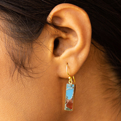 A close-up of a woman's ear wearing a 22k gold-plated dangle earring with a Mojave Brick gemstone from Vanya Lara.