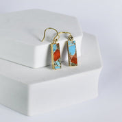 A pair of Mojave Brick earrings with blue and orange inlay on a white display stand, now with free shipping by Vanya Lara.