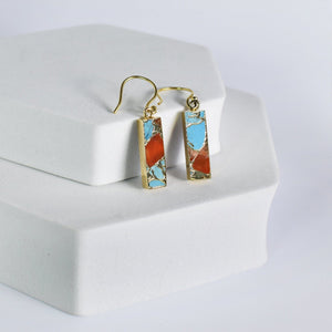 A pair of Mojave Brick earrings with blue and orange inlay on a white display stand, now with free shipping by Vanya Lara.