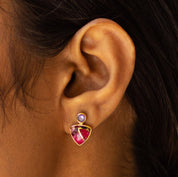 A close-up of a person's ear showcasing a triangle drop earring with gold plating and a small gemstone at the top by Vanya Lara.