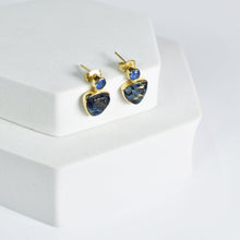 Load image into Gallery viewer, Triangle Drop Earrings with turquoise stones displayed on a white stand by Vanya Lara.
