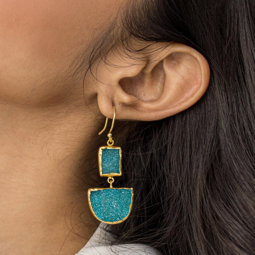 Close-up of a woman wearing Vanya Lara gold dangle earrings with blue Sugar Druzy stones.