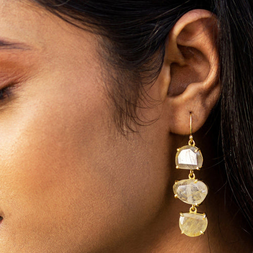 A close-up of a woman's ear showcasing Vanya Lara's Long Triple Drop Earrings with three yellow natural stones.