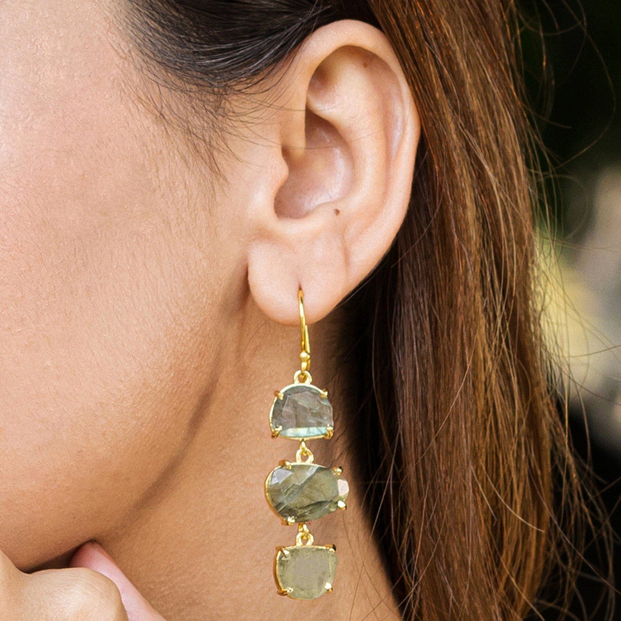 A close-up of a woman wearing Vanya Lara's Long Triple Drop Earrings with three green natural stones.