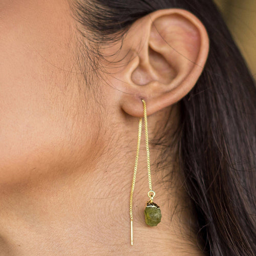 A close-up of a woman's ear wearing a Vanya Lara Pendulum Thread Earrings - VER0013 with adjustable dimensions and a green gemstone.