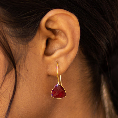 A close-up of a woman's ear wearing a Vanya Lara Beyond The Dainty Earrings - VER0014 with a red gemstone pendant.