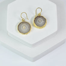 Load image into Gallery viewer, Pair of handcrafted gold-plated sliced quartz earrings by Vanya Lara displayed on a white stand.
