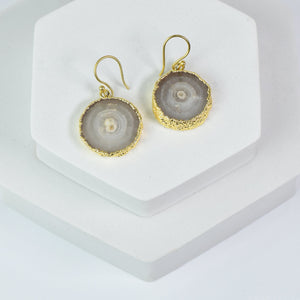 Pair of handcrafted gold-plated sliced quartz earrings by Vanya Lara displayed on a white stand.