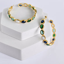 Load image into Gallery viewer, A Kaleidoscope Hoop Earrings set with green and blue hydro-stone gemstones on a white display stand by Vanya Lara.
