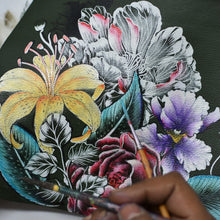 Load image into Gallery viewer, An artist&#39;s hand meticulously paints vibrant flowers, including a yellow lily and purple blooms, on the dark genuine leather surface of the exquisite Anuschka Zip-Top Shoulder Hobo - 707. Brushes and detailed floral patterns adorn the front of this elegant hobo bag, which features a chic chain detail shoulder strap.
