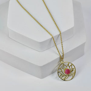 Golden Lotus Necklace by Vanya Lara with lotus detail and raw pink gemstones displayed on a white stand.