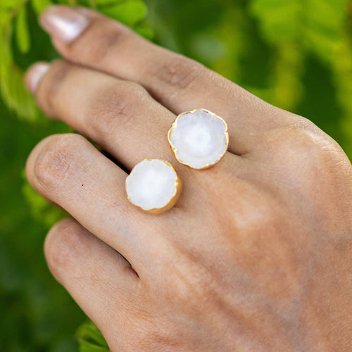 Hand wearing two Vanya Lara Solar Quartz Rings (VRG0001) with white gemstones against a green foliage background.