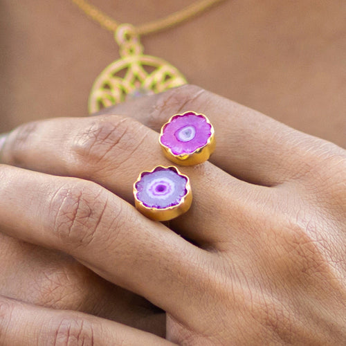A person displaying a pair of Vanya Lara gold rings with purple solar quartz gemstones.