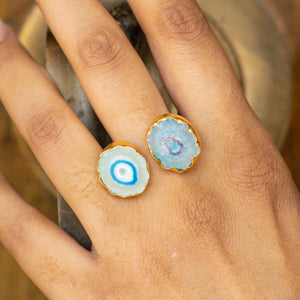 A hand displaying two Solar Quartz Rings from the Vanya Lara ring collection with blue agate gemstones against a natural backdrop, now available with free shipping.