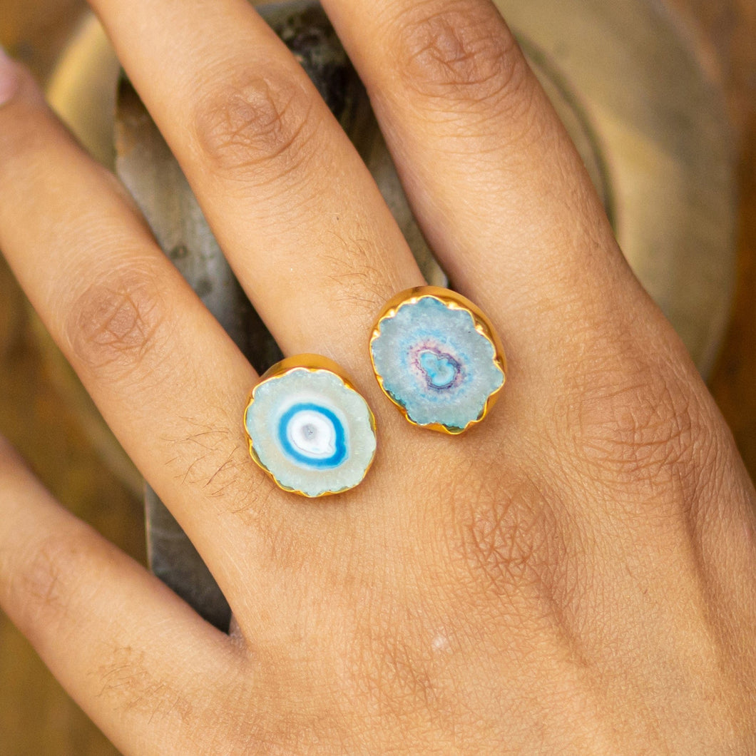 A hand displaying two Solar Quartz Rings from the Vanya Lara ring collection with blue agate gemstones against a natural backdrop, now available with free shipping.