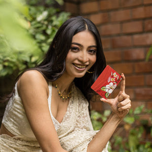 Woman smiling outdoors and showing a small leather credit card case with hand-painted floral artwork by Anuschka.