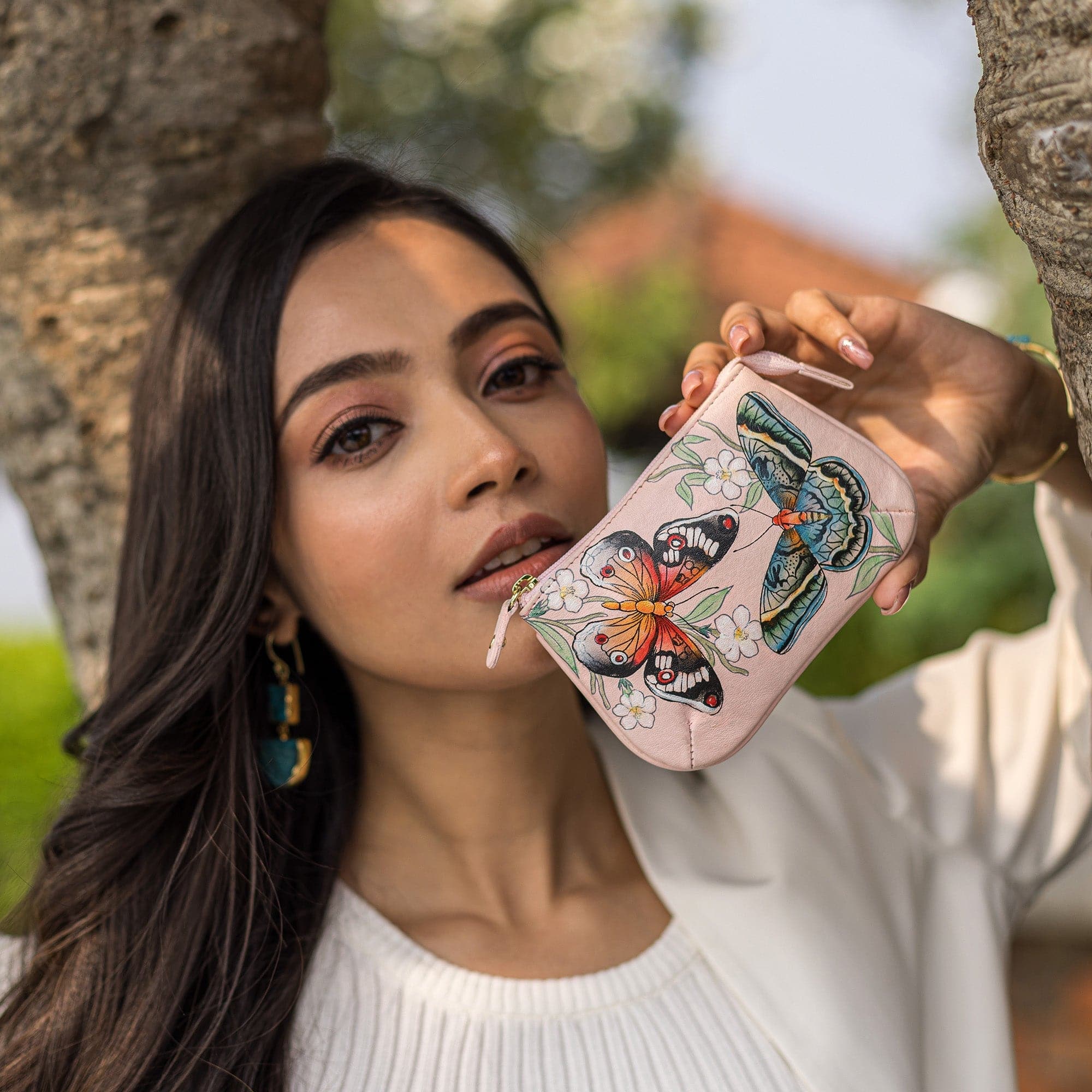 A woman showcasing a decorated leather Medium Zip Pouch - 1107 by Anuschka.