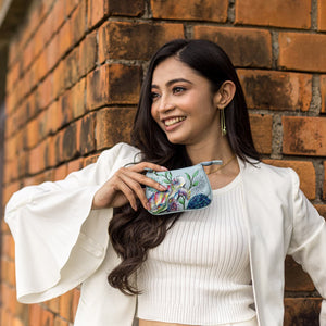 Woman smiling and holding an Anuschka Medium Zip Pouch - 1107 against a brick wall background.