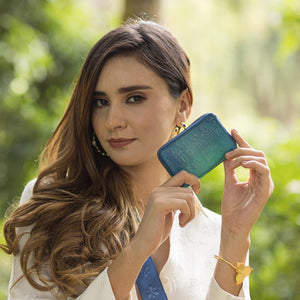 Woman holding up a small blue Anuschka Accordion Style Credit And Business Card Holder - 1110 outdoors.