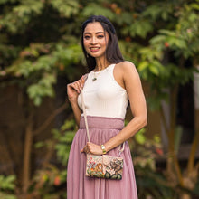 Load image into Gallery viewer, Woman in a sleeveless top and pleated skirt holding an Anuschka Cell Phone Case &amp; Wallet - 1113, posing outdoors.
