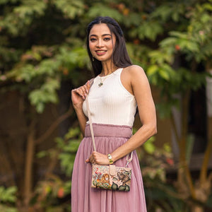 Woman in a sleeveless top and pleated skirt holding an Anuschka Cell Phone Case & Wallet - 1113, posing outdoors.