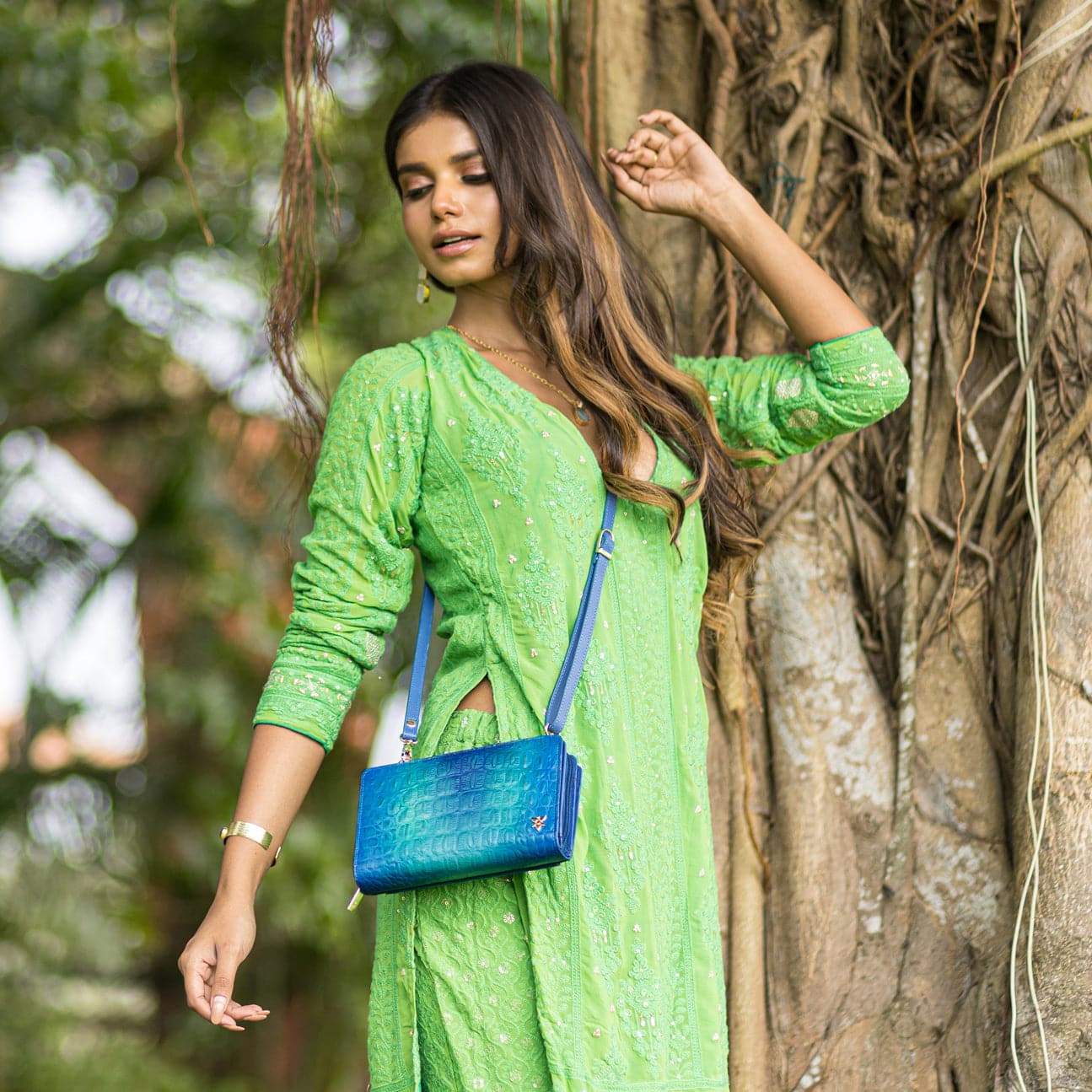 Woman in green traditional dress standing by a tree with an Anuschka Organizer Wallet Crossbody - 1149 featuring RFID protection.