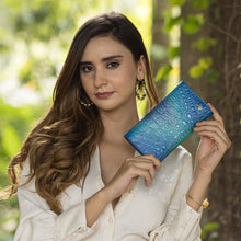 Load image into Gallery viewer, Woman holding a blue leather Three Fold Wallet - 1150 with RFID protection outdoors by Anuschka.
