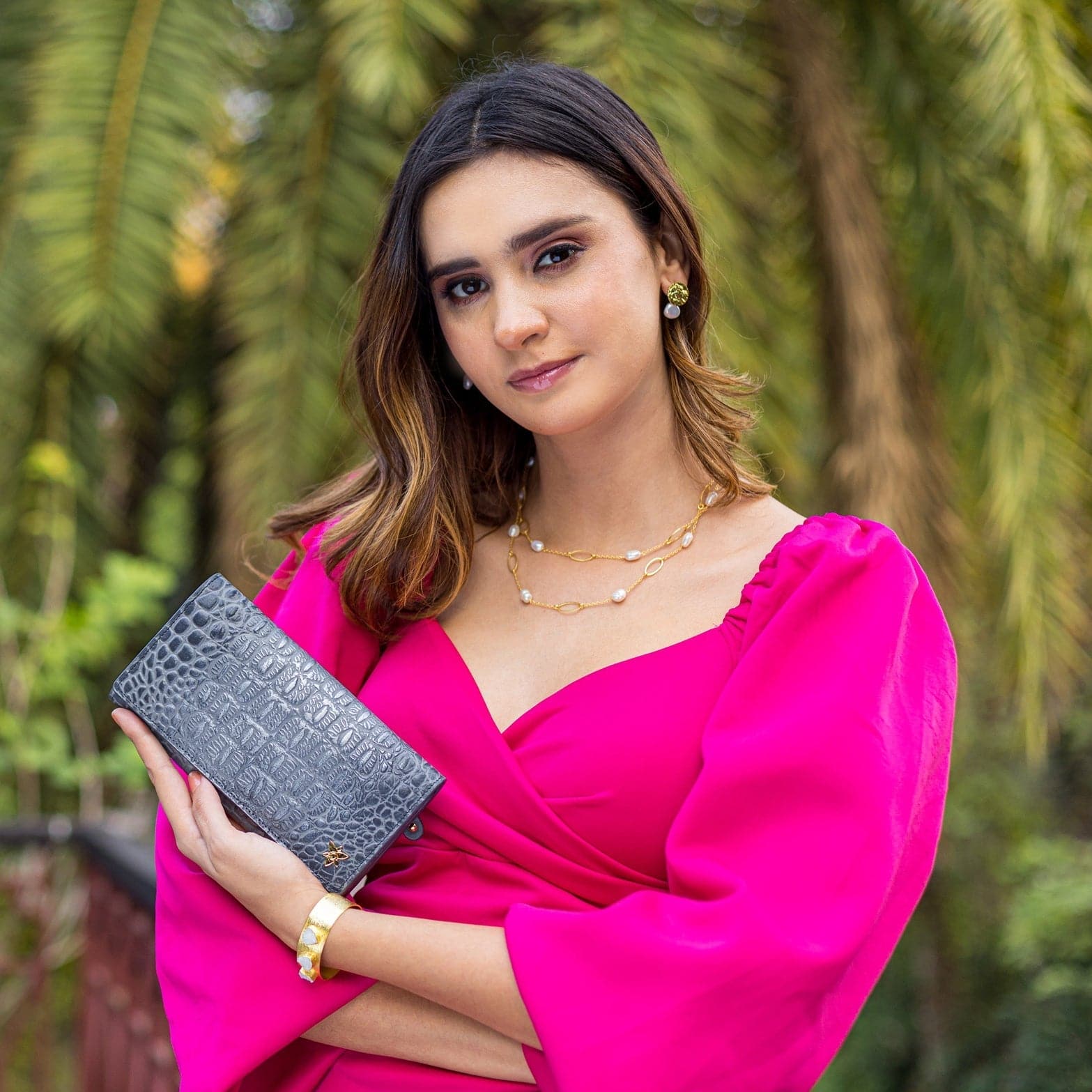 Woman in a pink dress holding a gray Anuschka Three Fold Wallet - 1150 clutch bag.