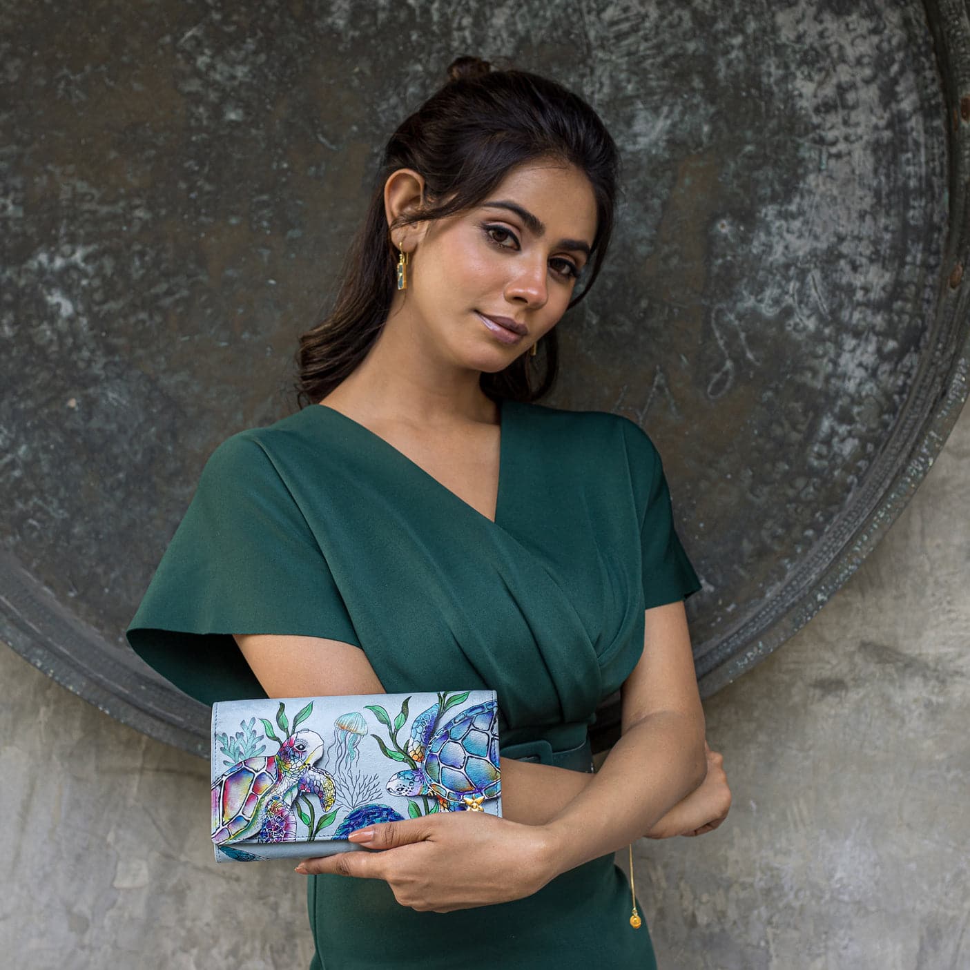Woman posing with a colorful, Anuschka Three Fold Wallet - 1150 against a textured background.