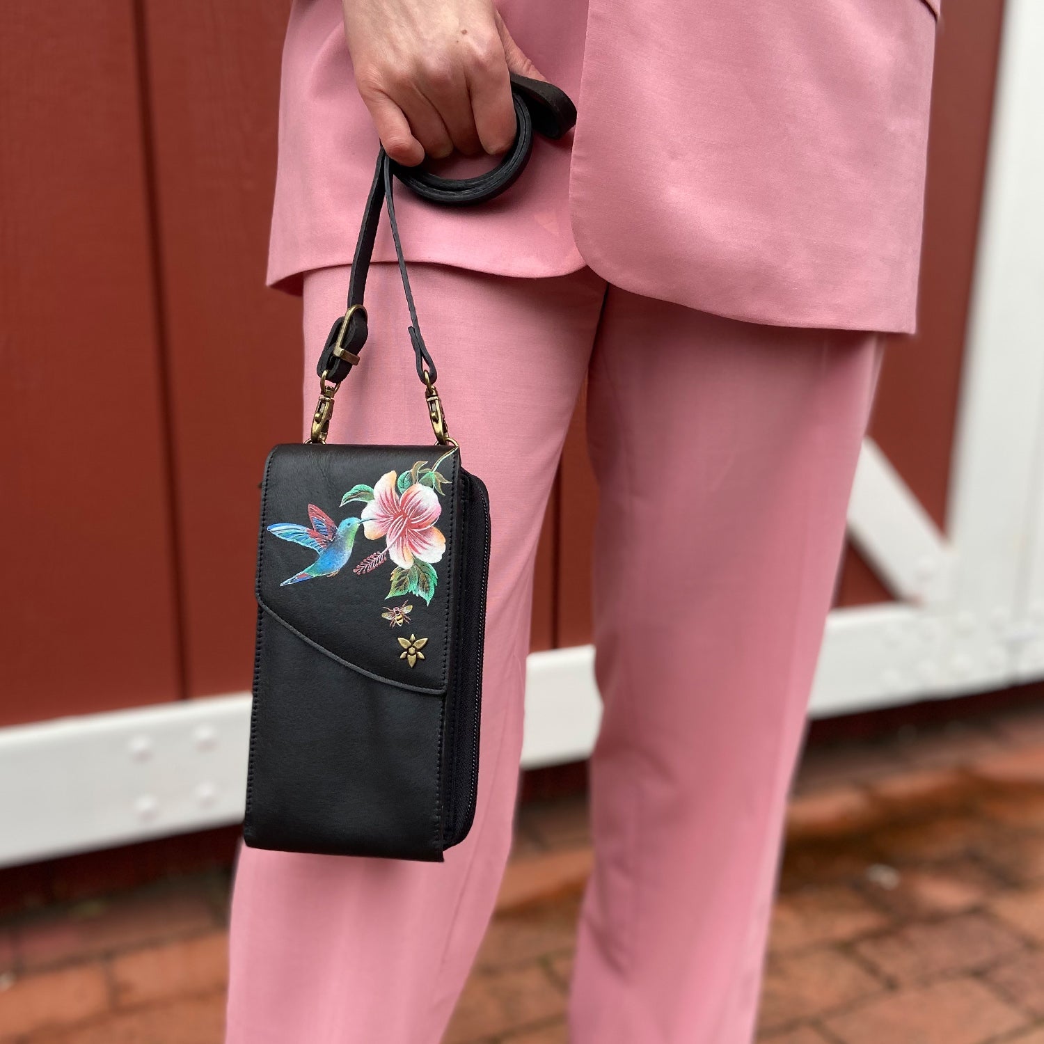 A person in a pink suit holding a black floral embroidered genuine leather Anuschka Crossbody Phone Case - 1173.