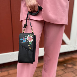 A person in a pink suit holding a black floral embroidered genuine leather Anuschka Crossbody Phone Case - 1173.