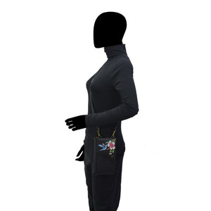 Side profile of a person wearing a black jumpsuit with floral embroidery and holding an Anuschka Crossbody Phone Case - 1173 made of genuine leather.
