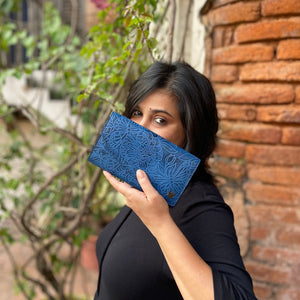 A woman holding a blue patterned Anuschka Accordion Flap Wallet - 1174 in front of her face while standing outdoors.