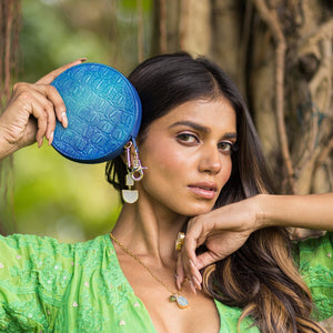 A woman holding a hand-painted, blue Round Coin Purse - 1175 by Anuschka and posing in a natural setting.