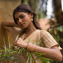 Load image into Gallery viewer, Woman in a beige dress posing with a focus on her traditionally designed, hand-painted Anuschka Leather Adjustable Leather Wrist Band - 1176.
